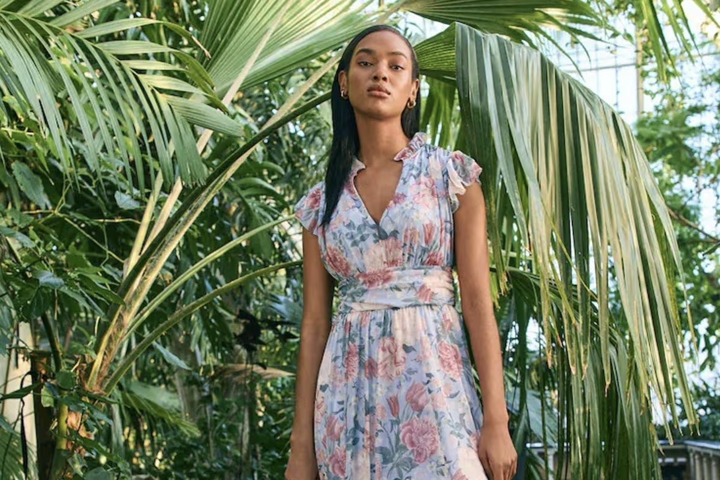 Model in een botanic-print jurk tussen palmbladeren